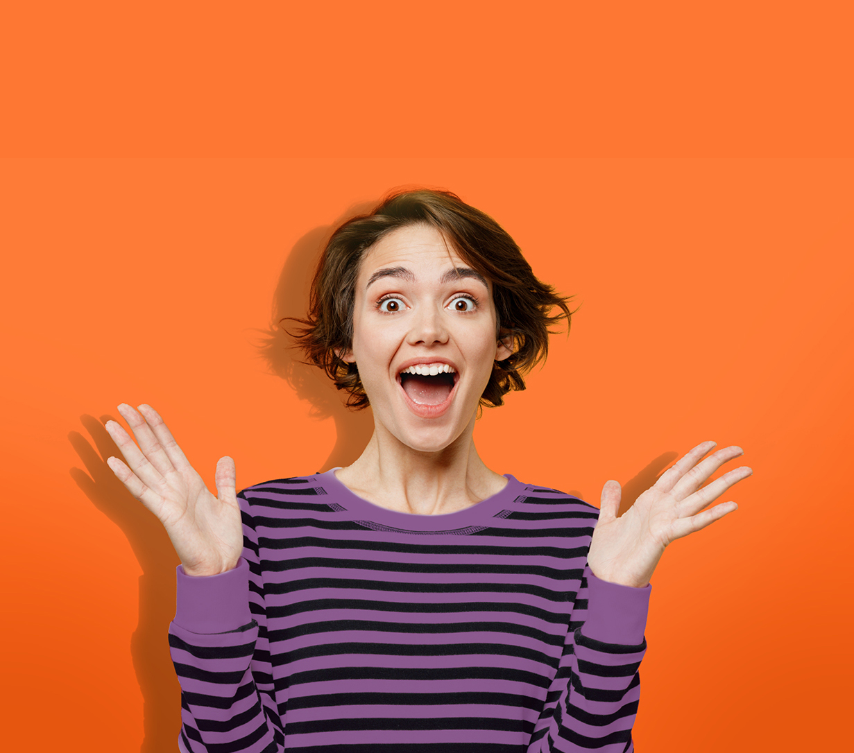 Die Abbildung zeigt eine strahlende, begeisterte junge Frau, die in einem lila/schwarz gestreiften Sweatshirt vor orangenem Hintergrund steht und beide Händen nach oben streckt
